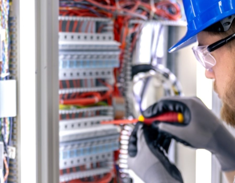 Male electrician in uniform working in a switchboard. Electricity.