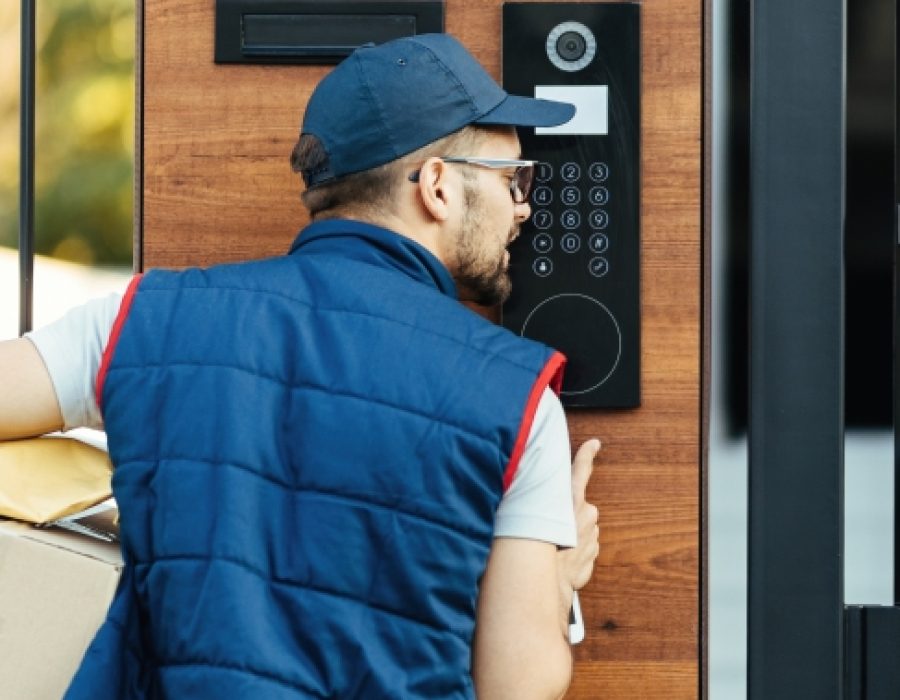 Rear view of a courier ringing on customer's intercom while making home delivery.